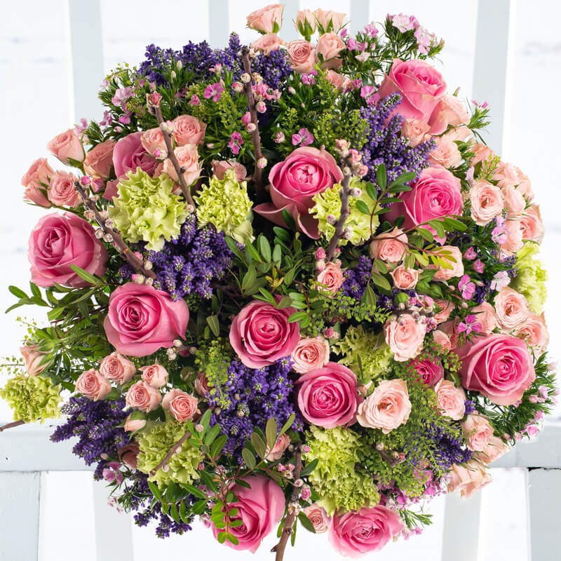 A large bouquet of real cherry blossom flowers, pink roses, green carnations, deep purple veronica, pink spray roses, and sweet Williams.